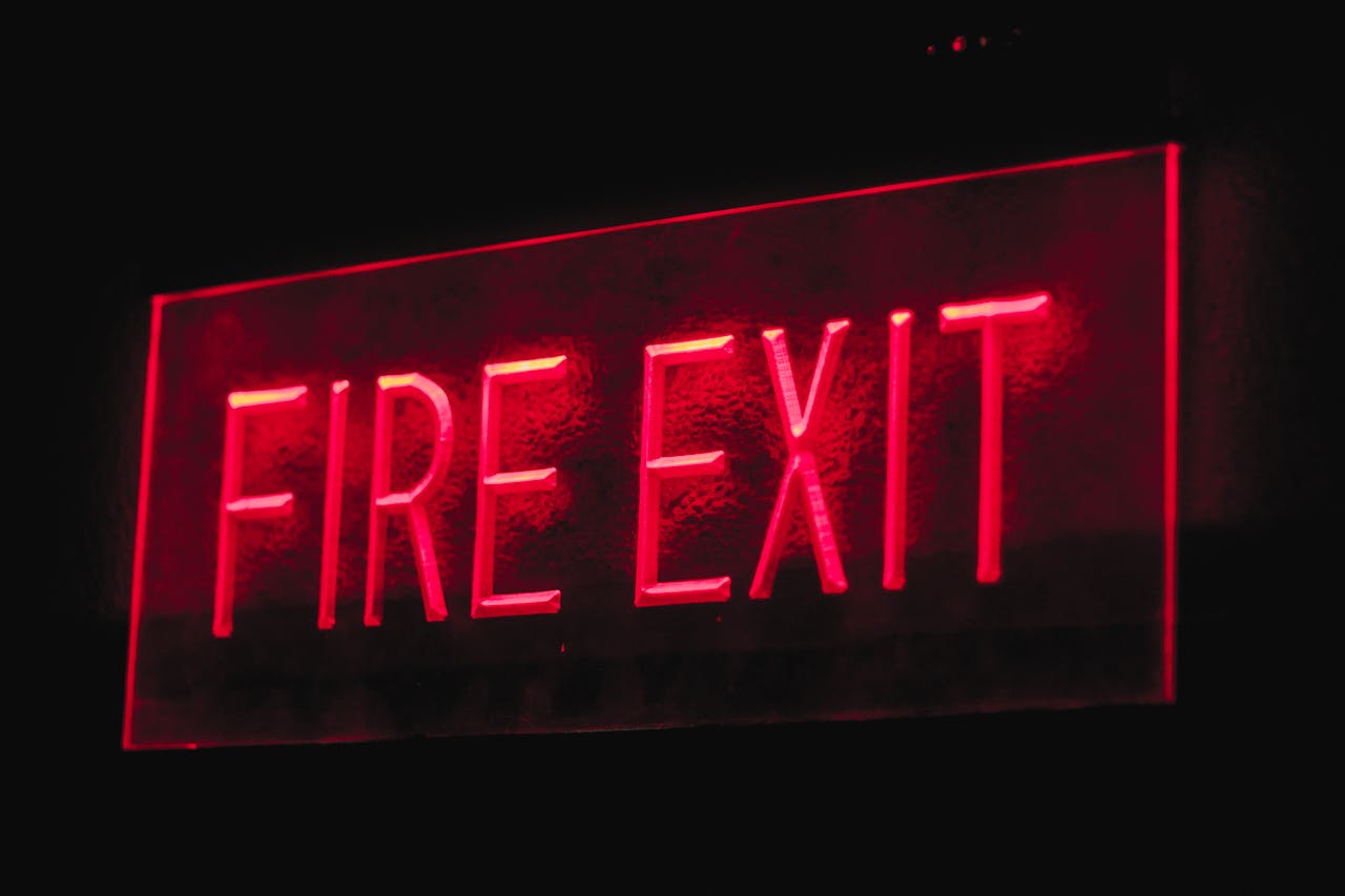 Brightly lit red neon fire exit sign illuminating in a dark setting.